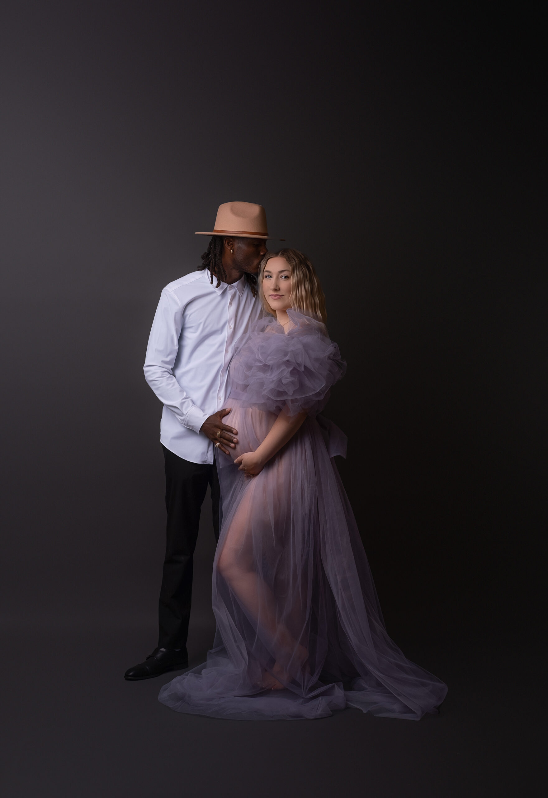 Expectant couple in elegant outfits posing for a maternity photoshoot in Calgary photography studio