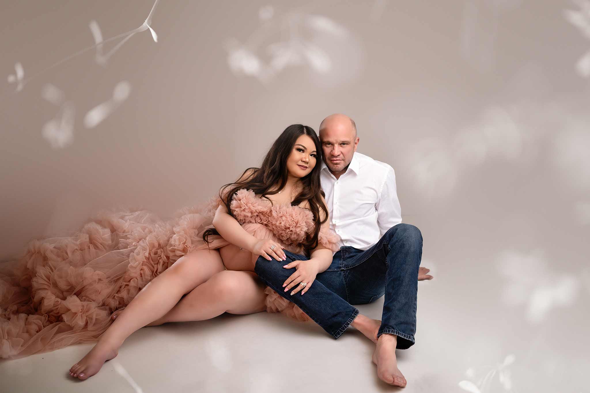 Husband and wife sitting on the floor during a maternity photo session in Calgary wearing a pink dress