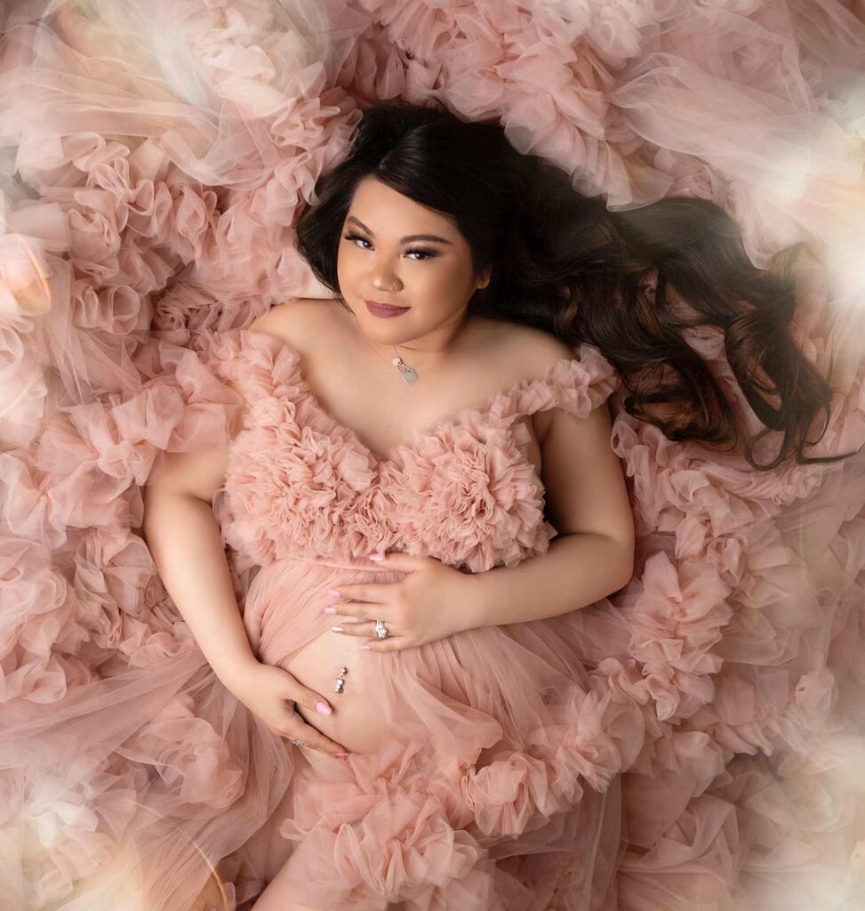 Calgary maternity photographer, pregnant woman showing belly laying on the floor with a fluffy pink dress