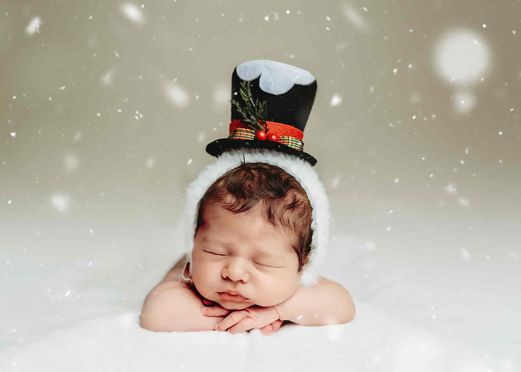 Newborn baby wearing a snowman Christmas hat for a studio photo session in Calgary, baby sleeping with chin on hands, snowy background