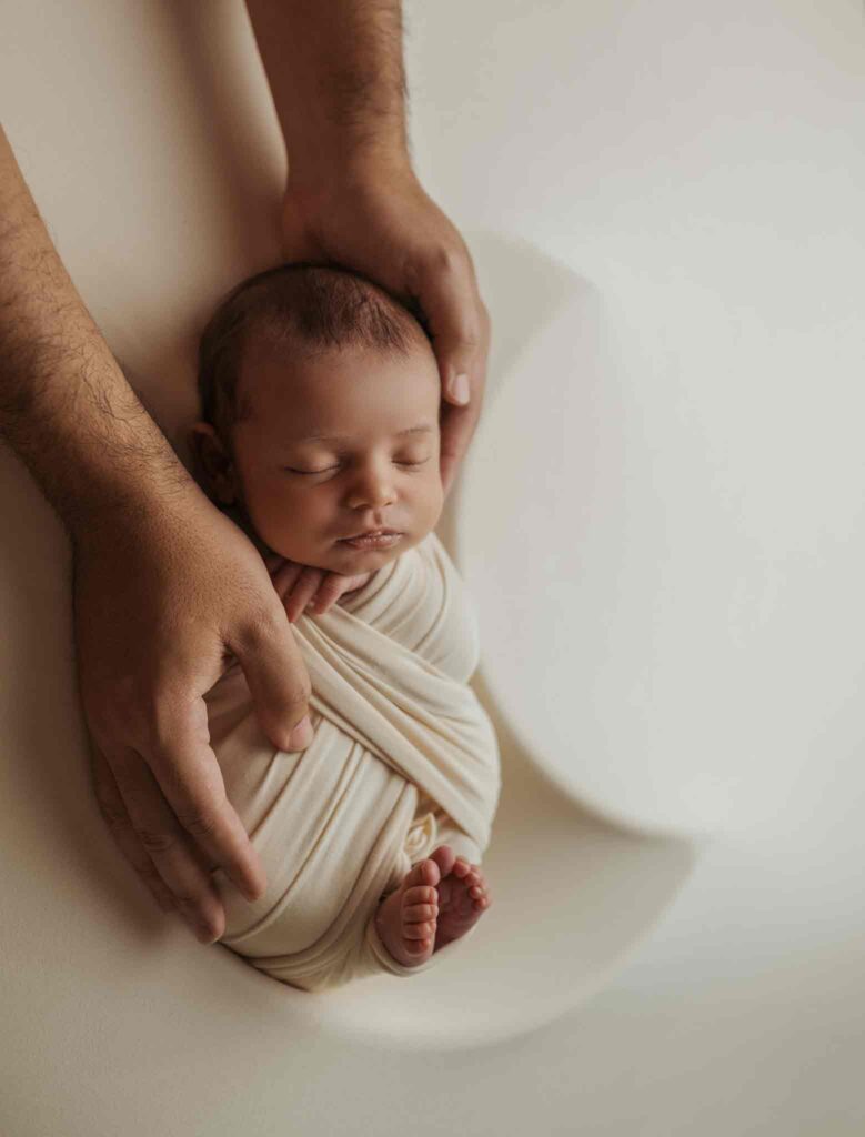 Calgary newborn photographer, baby sleeping in moon shaped bowl with daddy hands holding him