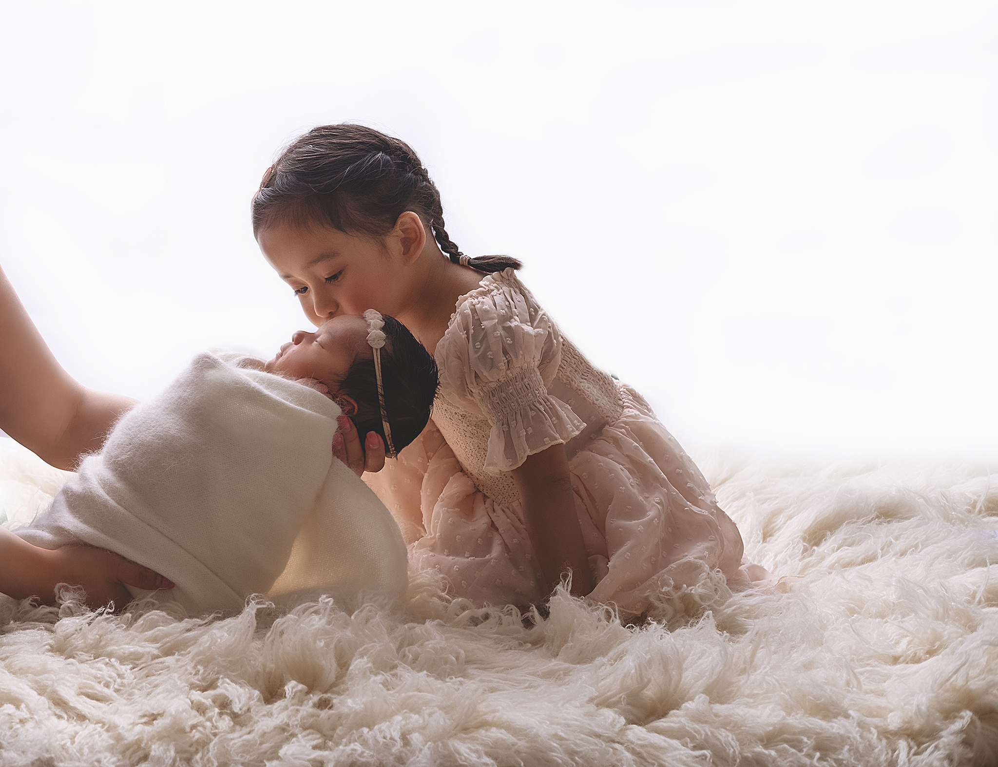 Newborn photography session in Calgary, siblings photos, big sister kissing baby sister in a white background