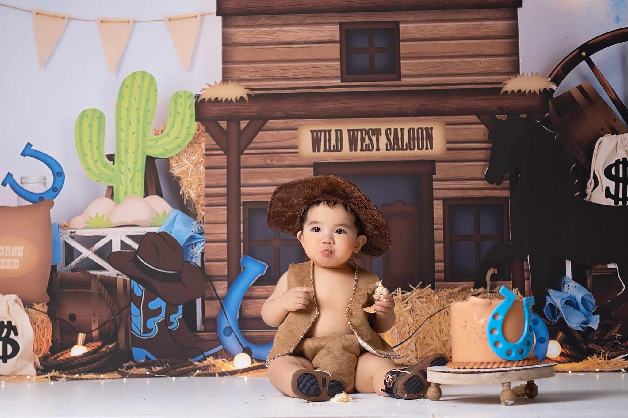 Baby boy riding a horse toy in his cake smash photoshoot, stampede theme