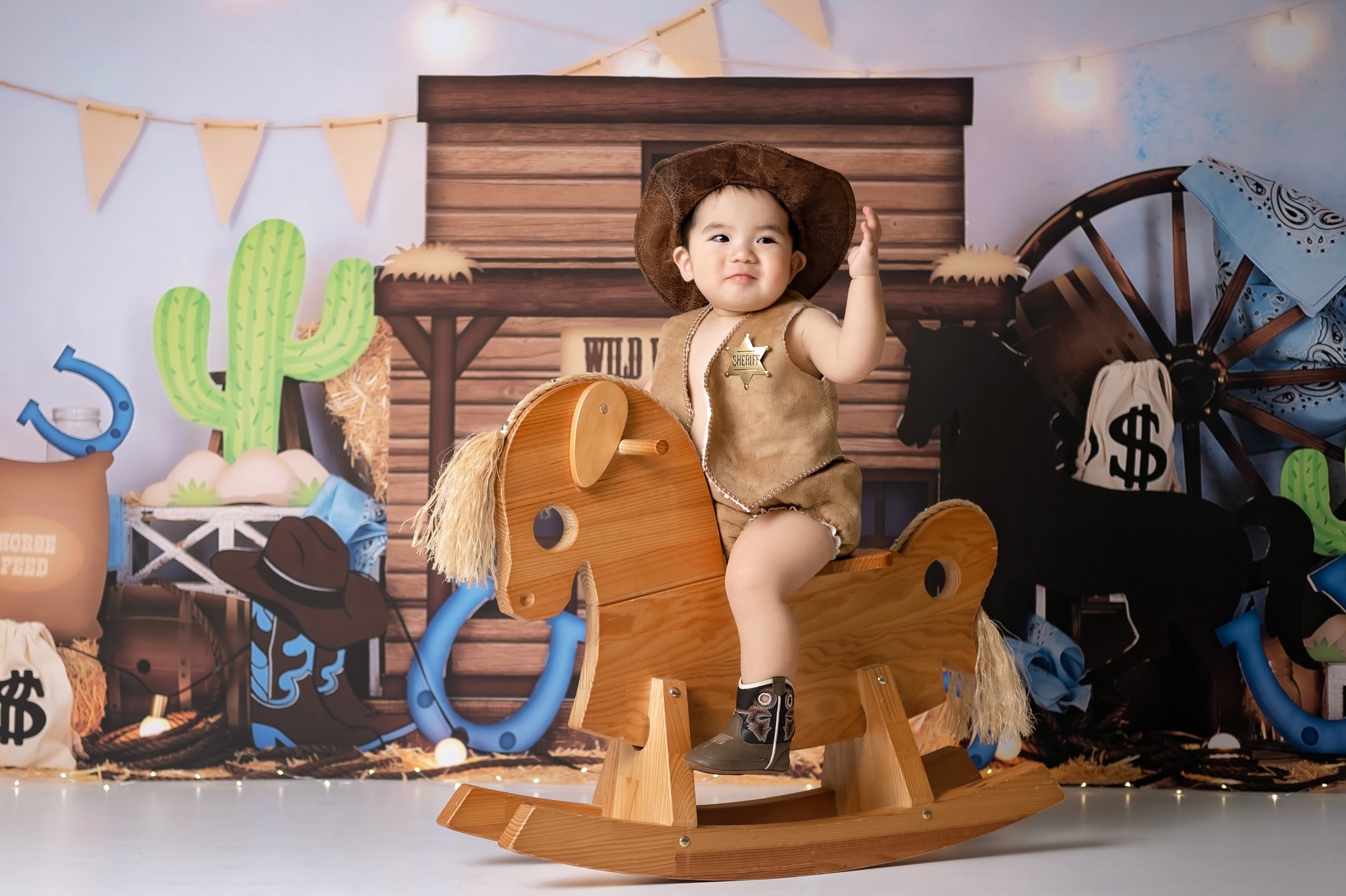 Baby boy riding a horse toy in his cake smash photoshoot, stampede theme