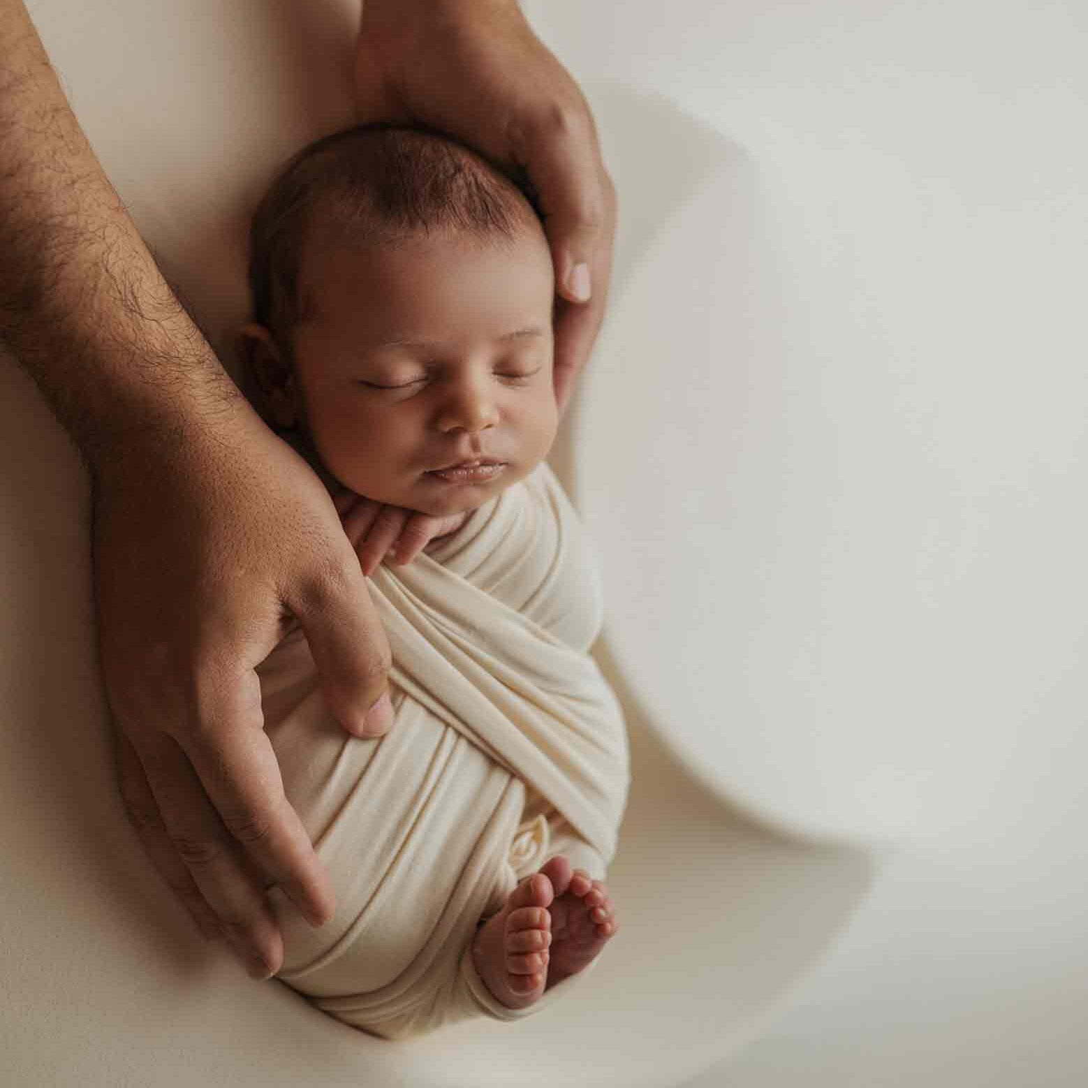 Calgary newborn photographer, baby sleeping in moon shaped bowl with daddy hands holding him