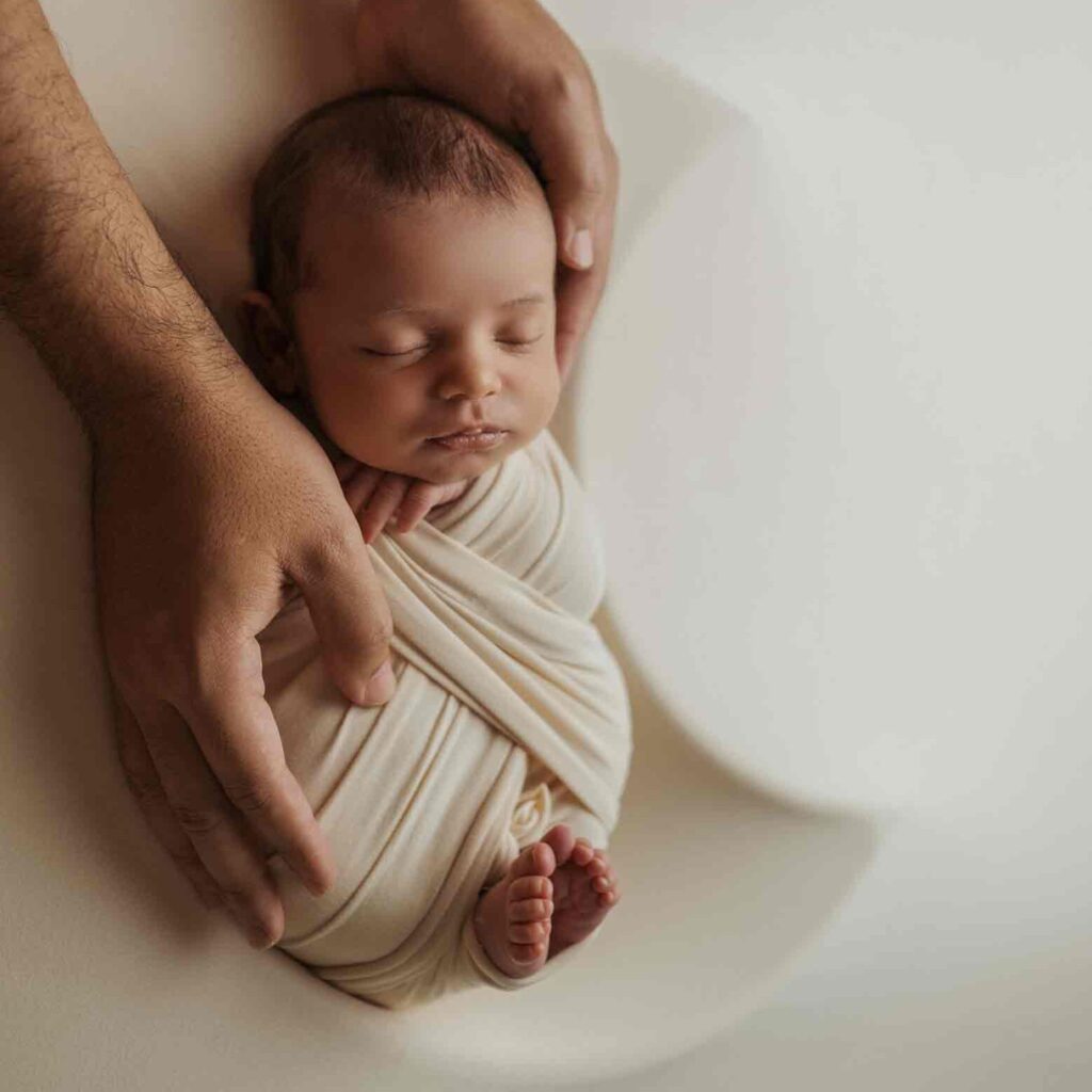 Calgary newborn photographer, baby sleeping in moon shaped bowl with daddy hands holding him